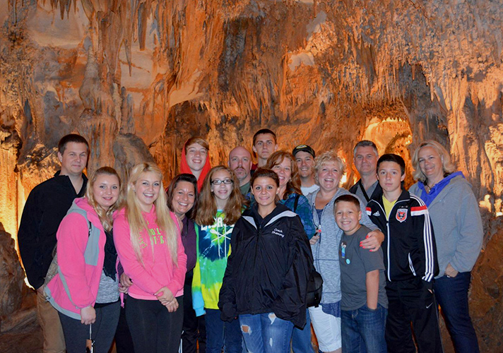 Large group of 16 people looking to the camera with illuminated cave walls behind them.