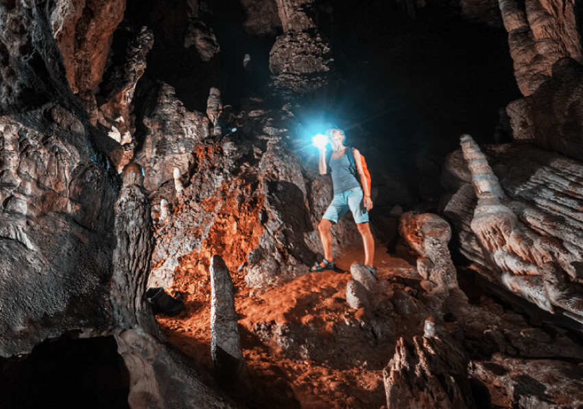 A person standing inside of a cavern looking up at the ceiling while holding a flashlight towards you.