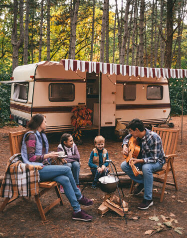 Happy family on a camping trip relaxing in the autumn forest. Camper trailer. Fall season outdoors trip.