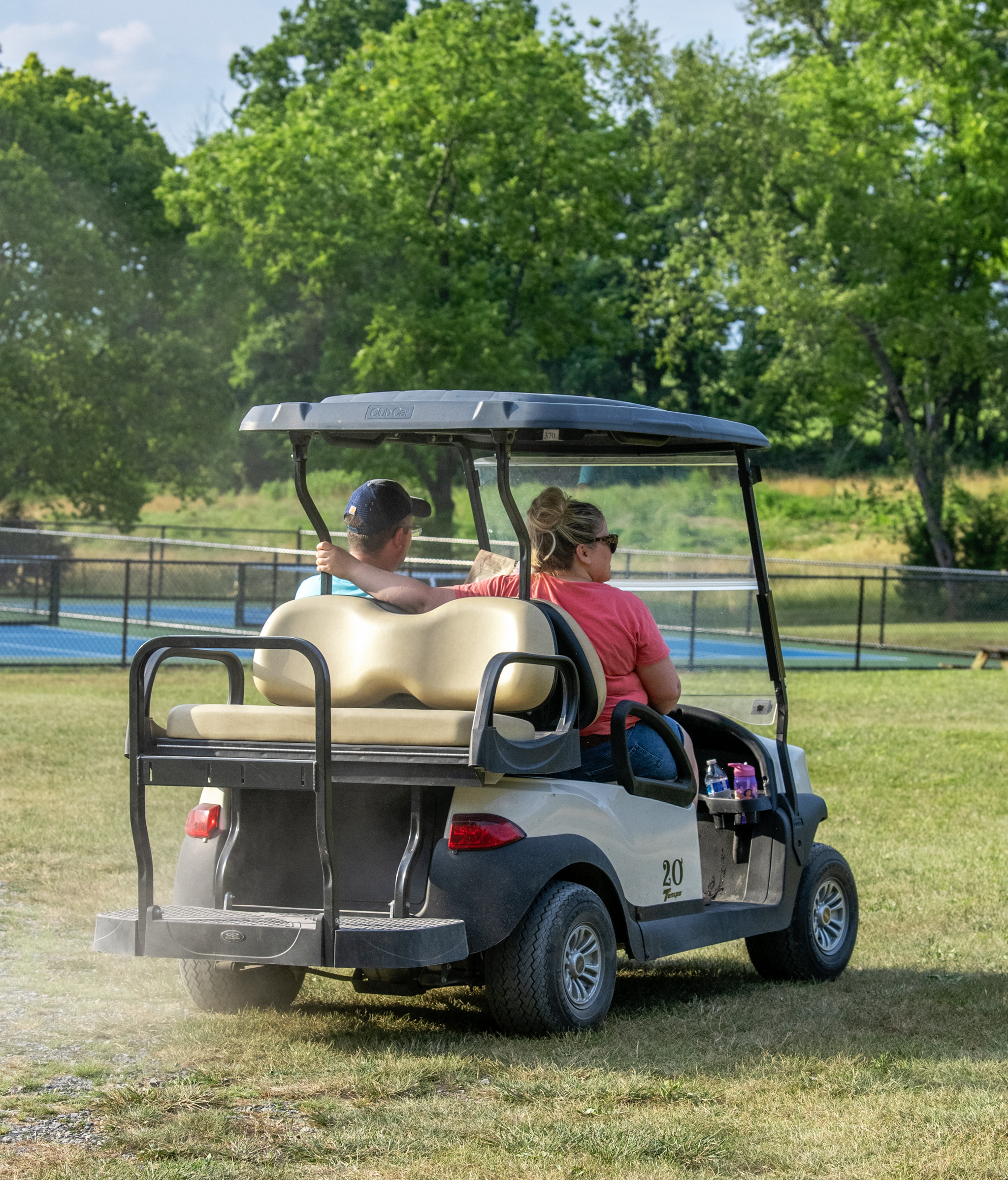 Couple driving on golf cart with pickleball courts in background